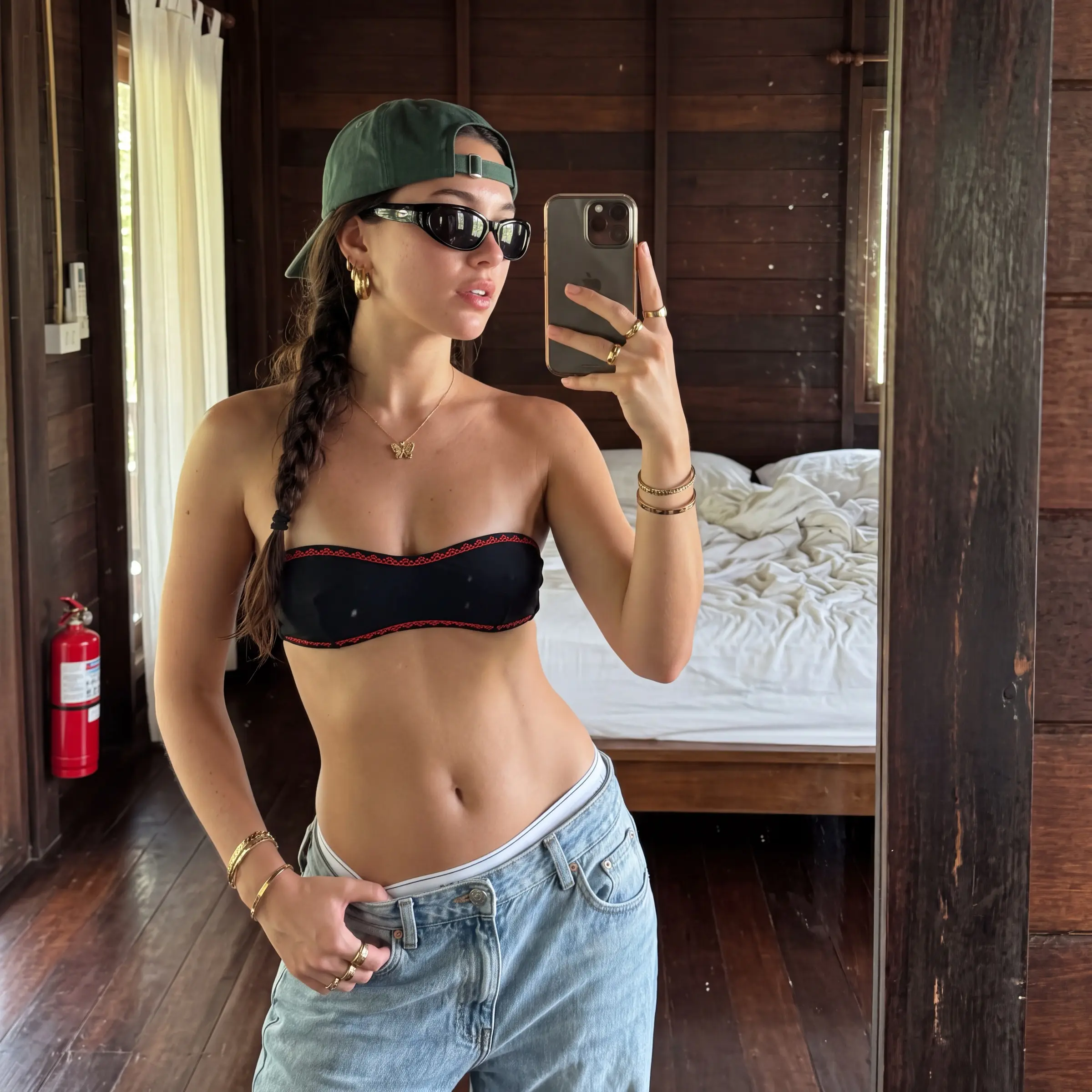 Woman in a backwards cap and baggy jeans taking a mirror selfie in a wooden bungalow