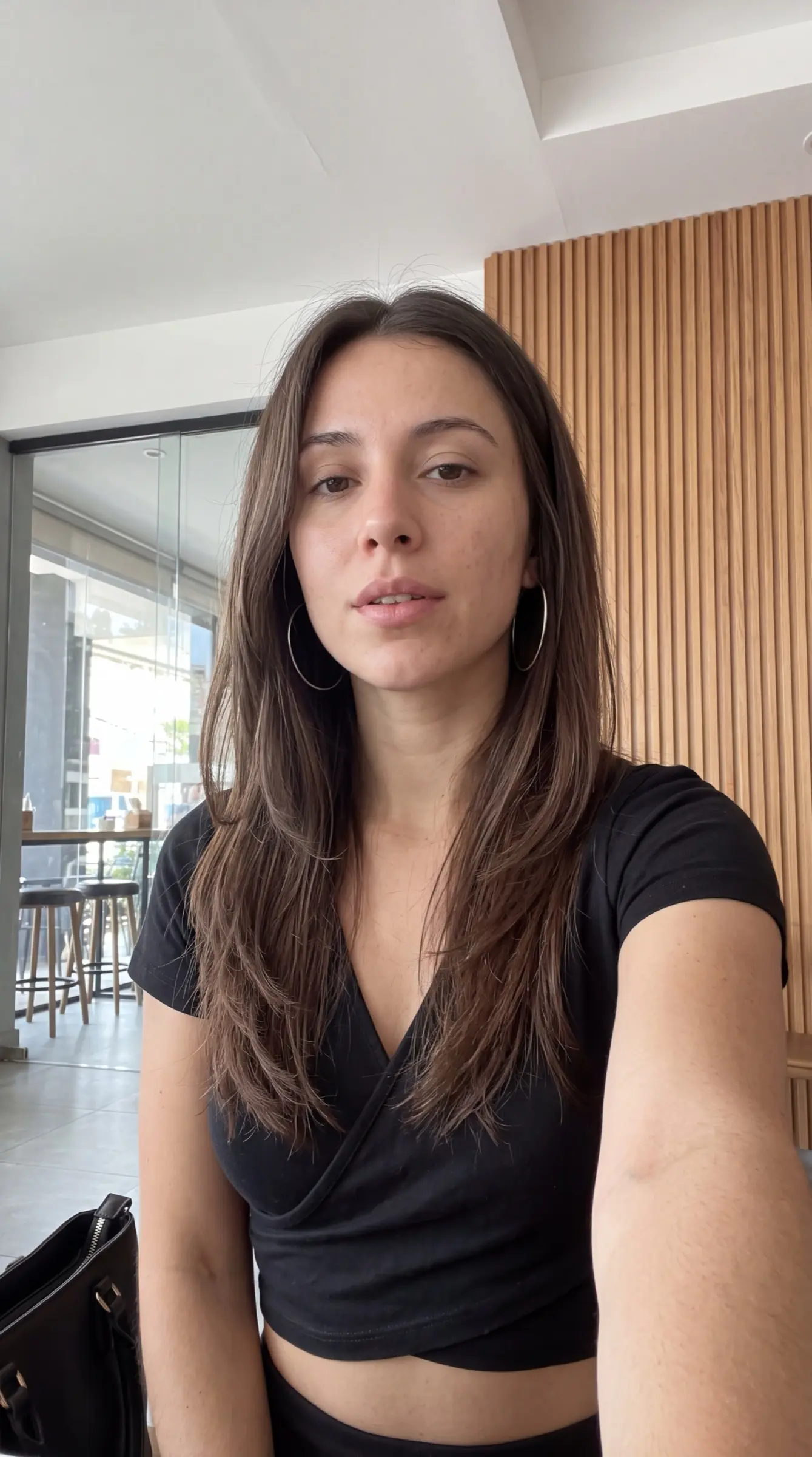 Woman in a black wrap top taking a close selfie in a wood-panelled hallway