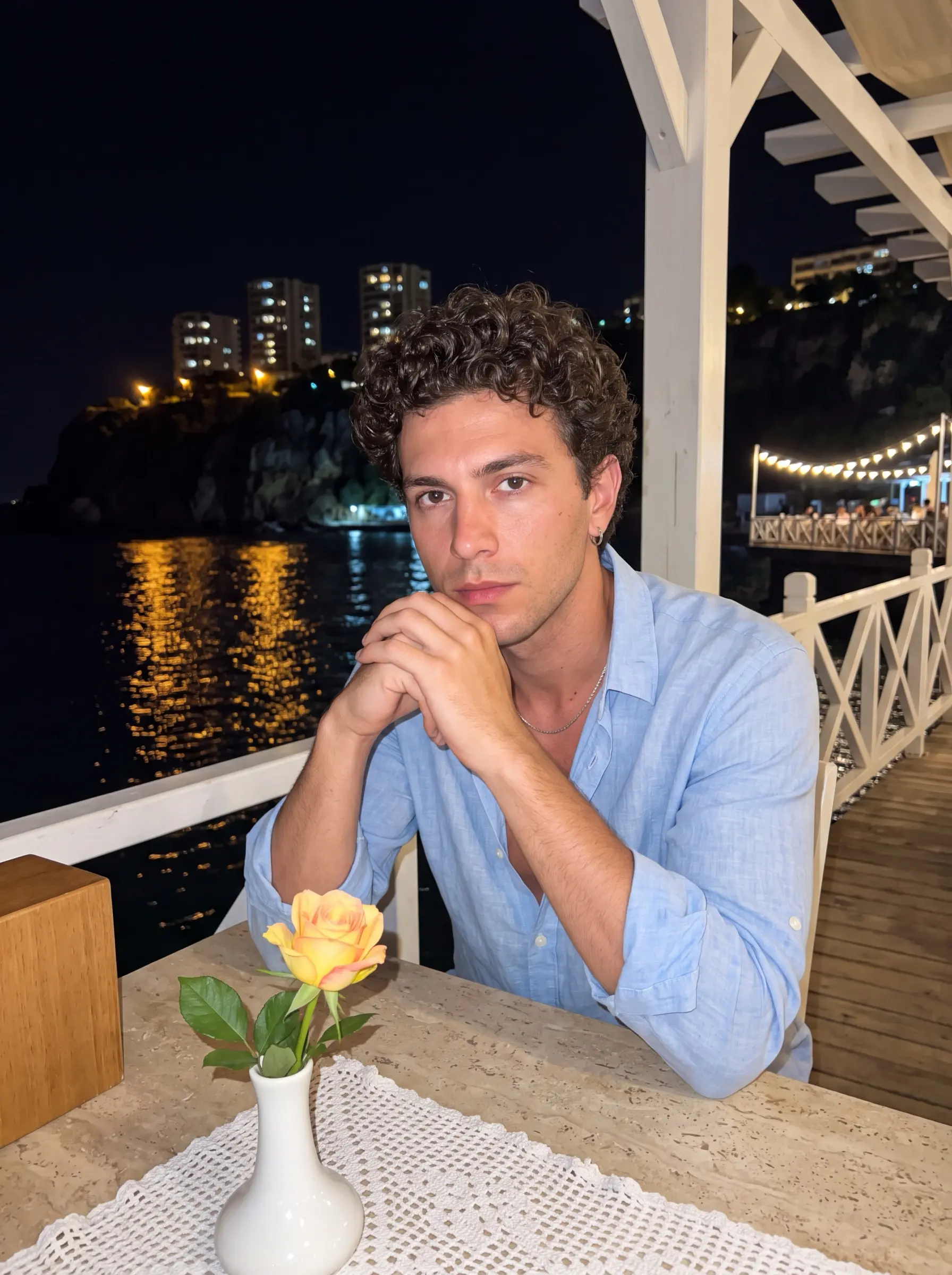 Man in a light blue linen shirt sitting at a pier restaurant table at night